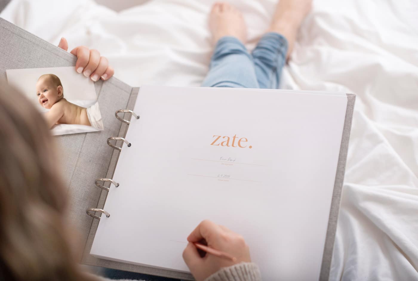 Dojenčkov album Zate Ženska drži v rokah dojenčkov album Zate v sivi barvi in ga izpolnjuje